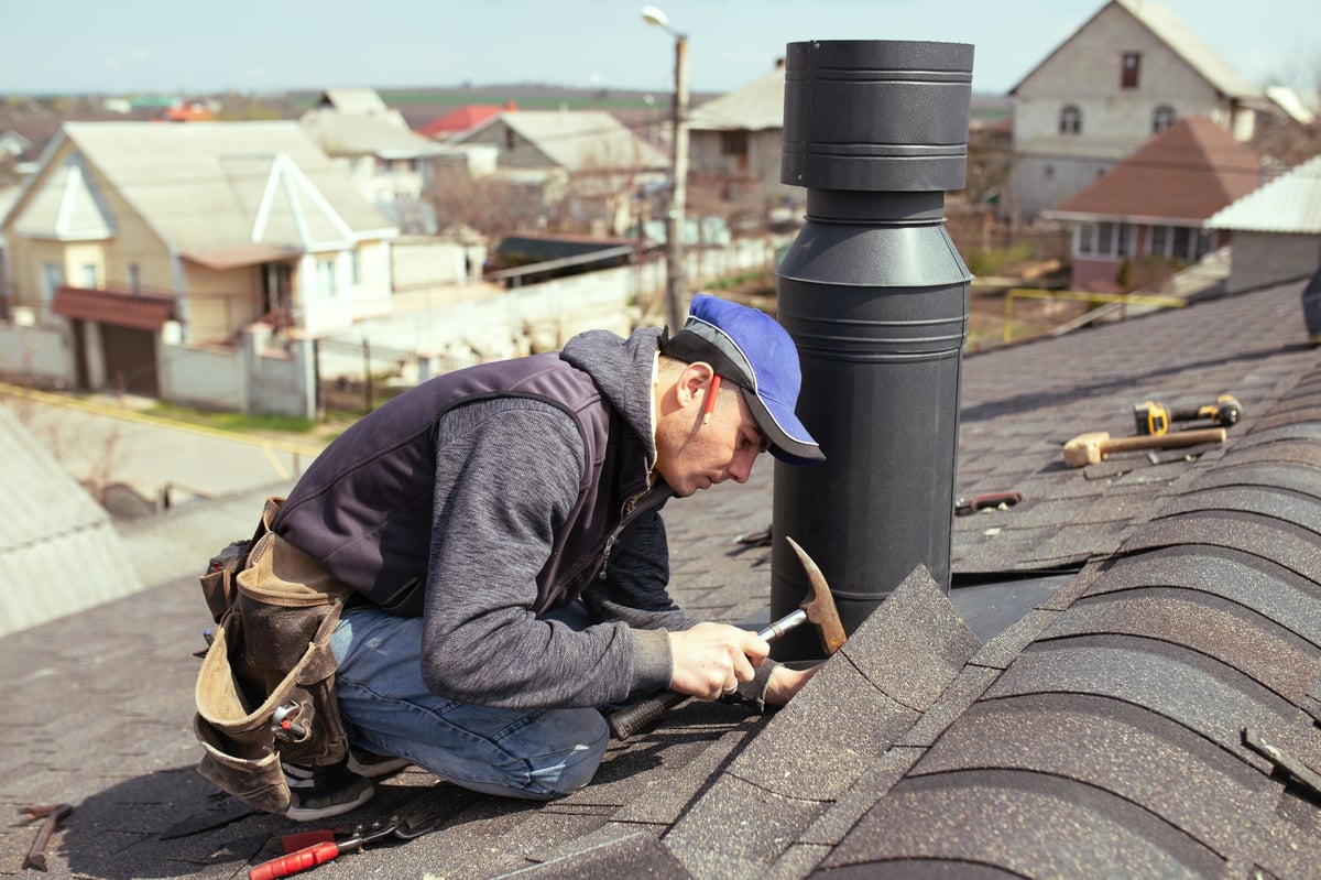 a professional master roofer with hammer repairs the roof. Repair Asphalt Shingles or Bitumen Tiles on the Rooftop Outdoor