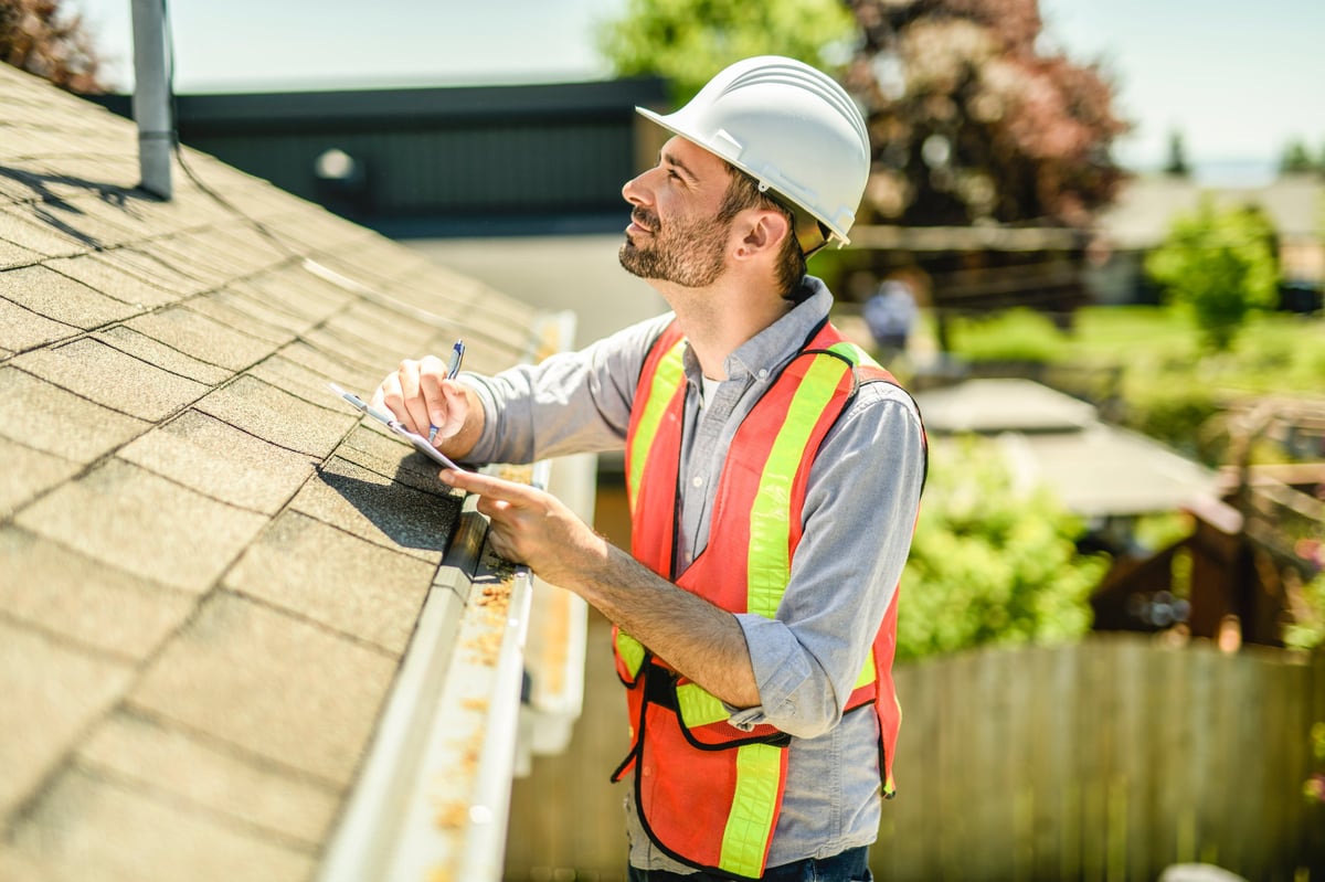 A man with a white hard hat holding a clipboard, inspect house